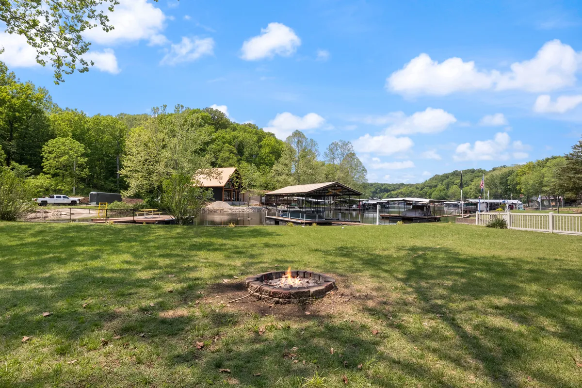 An exterior shot featuring a cozy fire pit area by the waterfront, surrounded by greenery and a dock. The scene invites guests to enjoy evening campfires, s'mores, and lakeside conversations.
