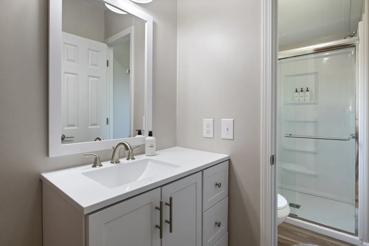 A fresh, modern bathroom with a vanity, sink, mirror, and a spacious shower area. The color palette is calm and neutral, evoking relaxation and privacy—ideal for personal routines during group stays.