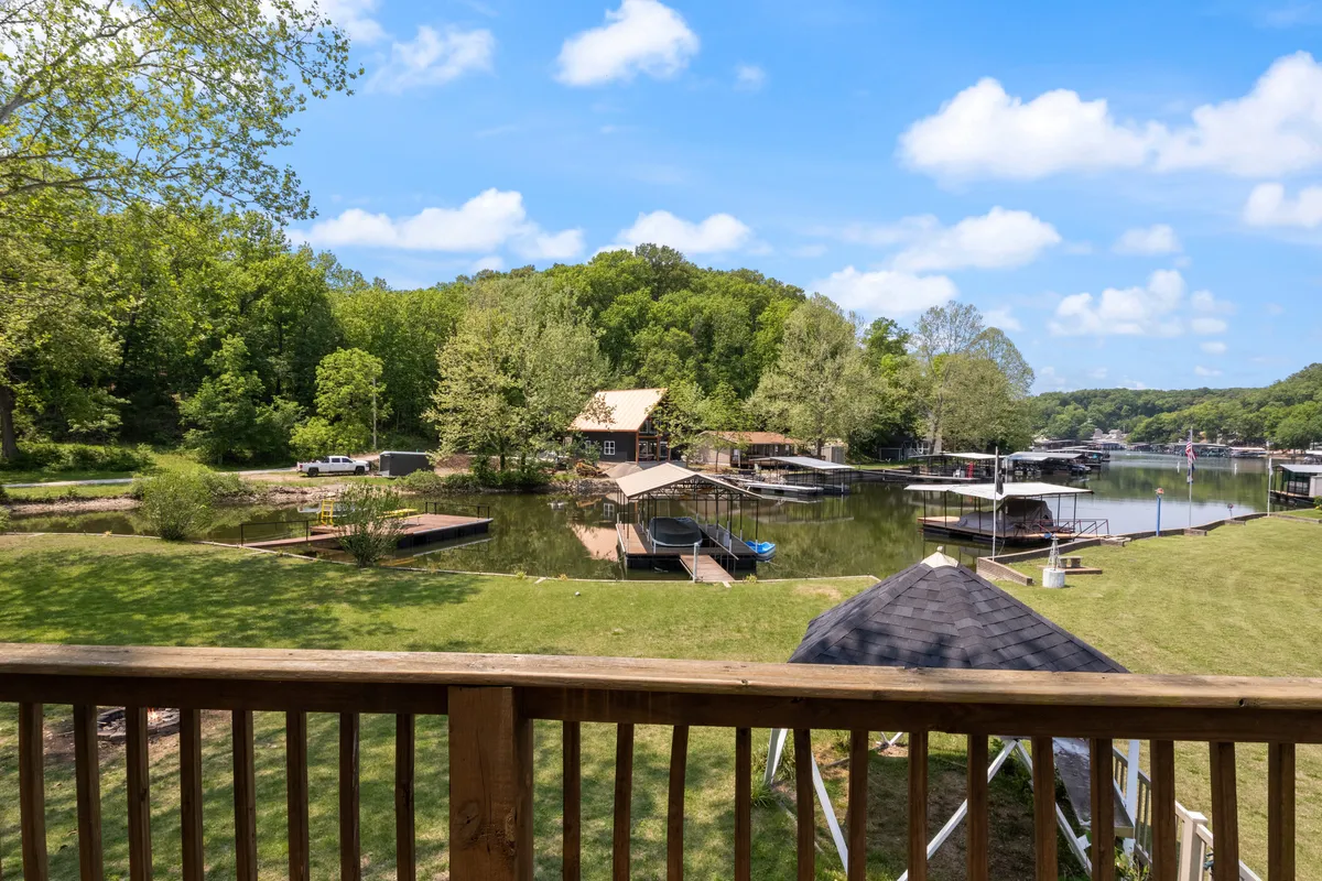 A tranquil view features calm blue waters, dock structures, and rich greenery along the shoreline beneath a sky dotted with soft clouds. The landscape suggests opportunities for boating, water sports, nature walks, and picnics in a peaceful natural setting.