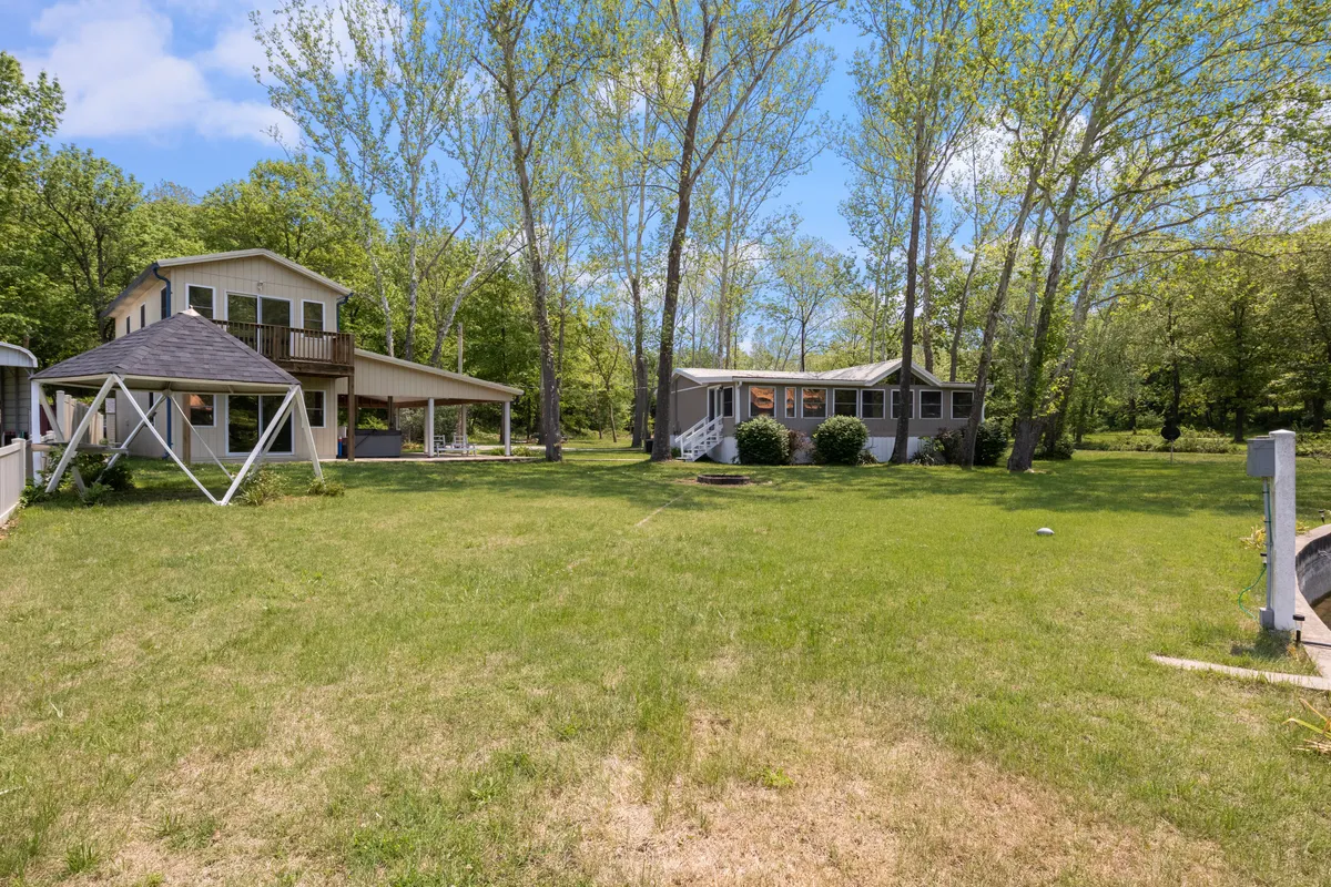 A broad view of the two homes set on a lush green lawn, surrounded by tall trees. The homes are separate but close, highlighting both privacy and togetherness for larger groups. The setting suggests plenty of space for outdoor games, lounging, and enjoying nature as a group.