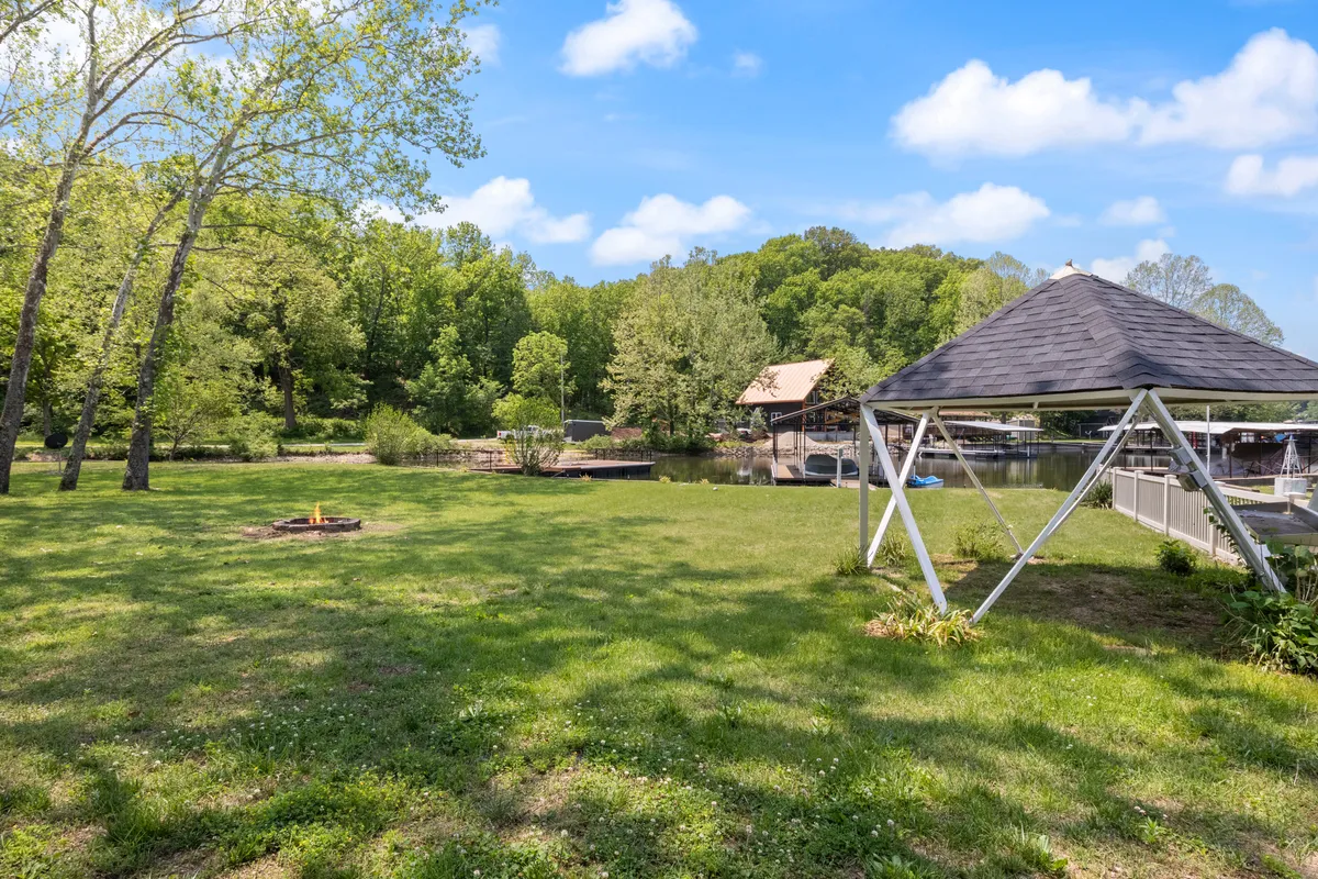 A peaceful lakeside setting featuring a charming gazebo, a fire pit, and lush greenery bordering the water. The setup invites guests to relax, enjoy fishing or boating, and gather around the fire in the evening as the sun sets over the lake.