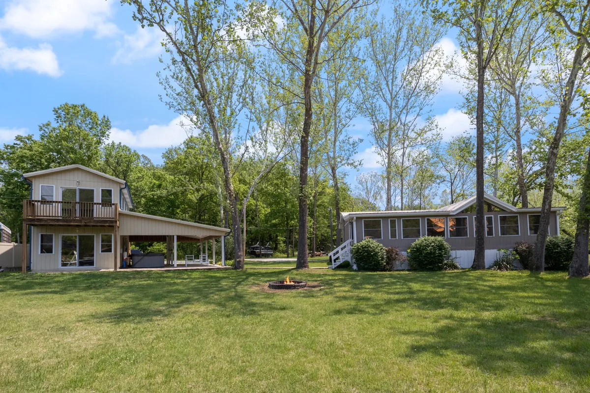 This image shows two separate houses on a shared lot, surrounded by lush greenery with a fire pit area between them. The exteriors of both homes are clearly visible, conveying the concept of two distinct, private residences within a single property.