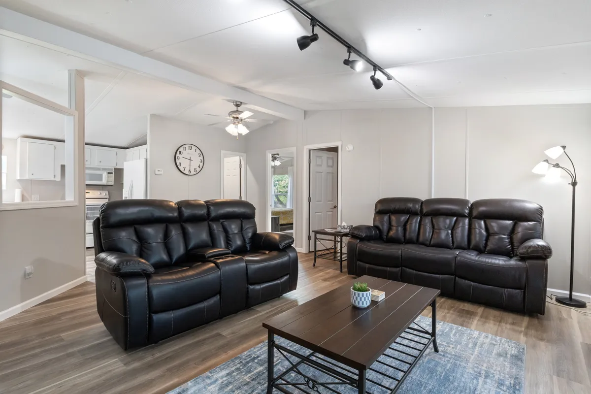 A cozy living area featuring black reclining sofas, a wooden coffee table, a floor lamp, and a decorative plant. The space is ideal for relaxation, group gatherings, or quiet moments, giving a sense of privacy and personal comfort.