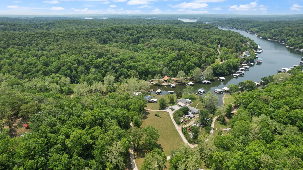 A tranquil exterior view featuring a lush green forest and a serene waterway, with scattered homes and dirt paths leading to the water. The scene invites exploration, relaxation, and a sense of escape from urban life.