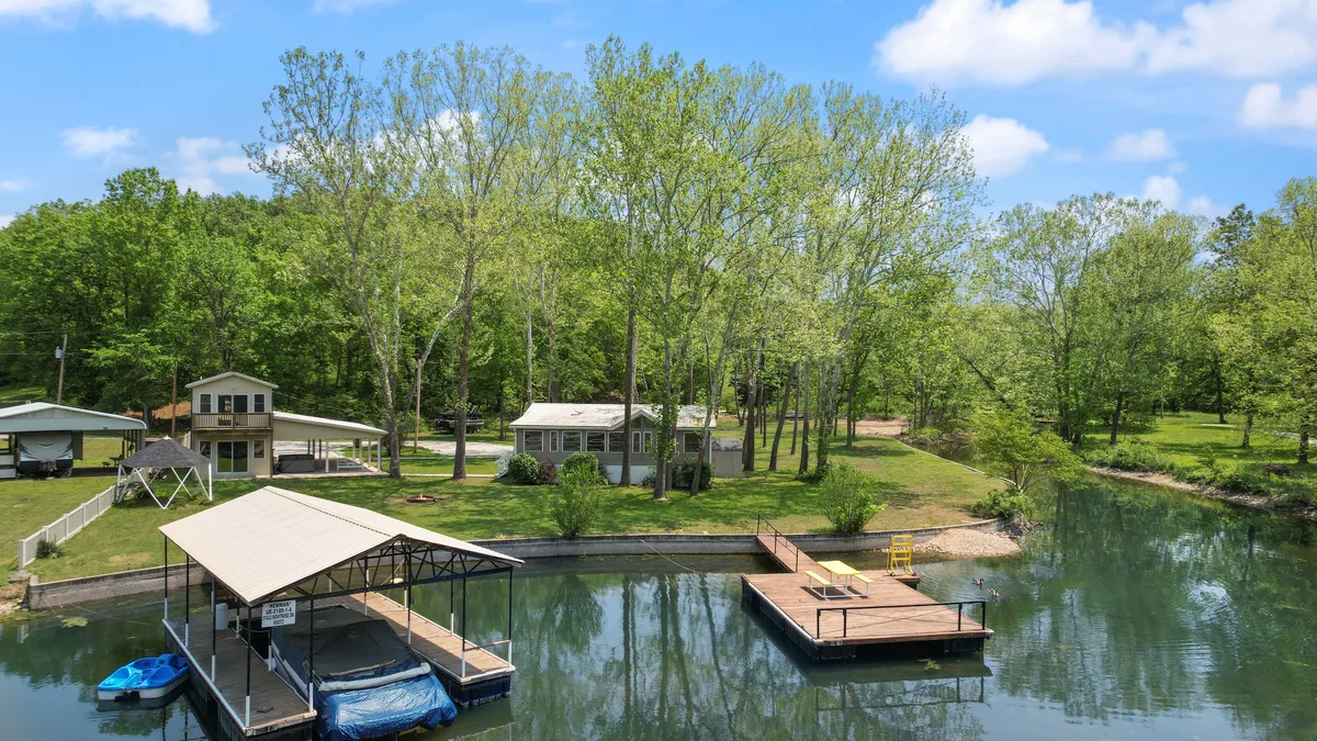 A view of the house and its private boat dock along a quiet canal, surrounded by lush trees. The tranquil water and dock offer opportunities for boating, sunset views, and waterfront relaxation, making it ideal for social activities and lakeside barbecues.