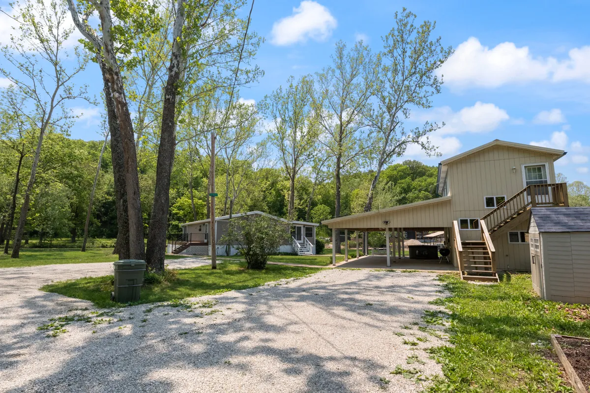 This exterior scene features tall trees, a driveway, and a green lawn surrounding homes. It conveys a tranquil, community feel with plenty of space for outdoor gatherings, family barbecues, or peaceful walks.