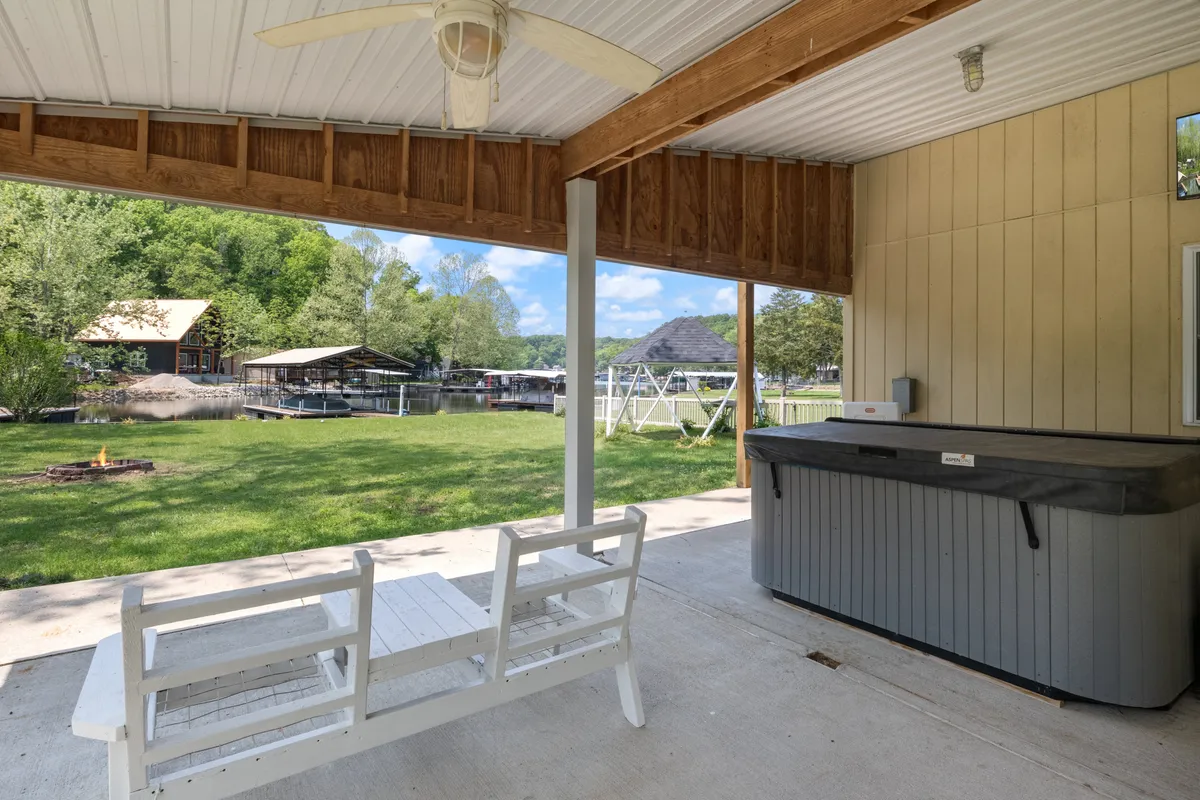A bubbling hot tub sits on a wooden patio overlooking a spacious green lawn. A swing set and bench are visible, emphasizing family-friendly fun and relaxation. The lawn provides plenty of room for outdoor games or picnics, and the hot tub invites guests to unwind as evening falls.