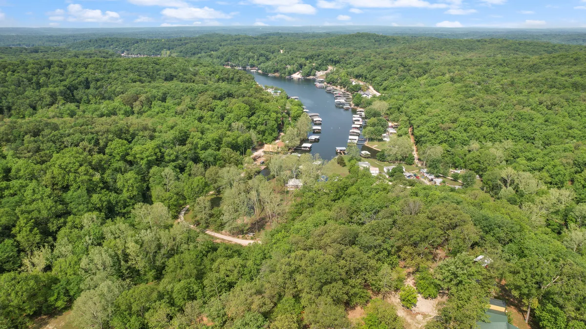 A serene winding river bordered by dense forest, with a few boathouses dotting the shoreline. The calm water and lush greenery evoke a sense of peacefulness, inviting visitors to enjoy outdoor activities like fishing, boating, and wildlife spotting.