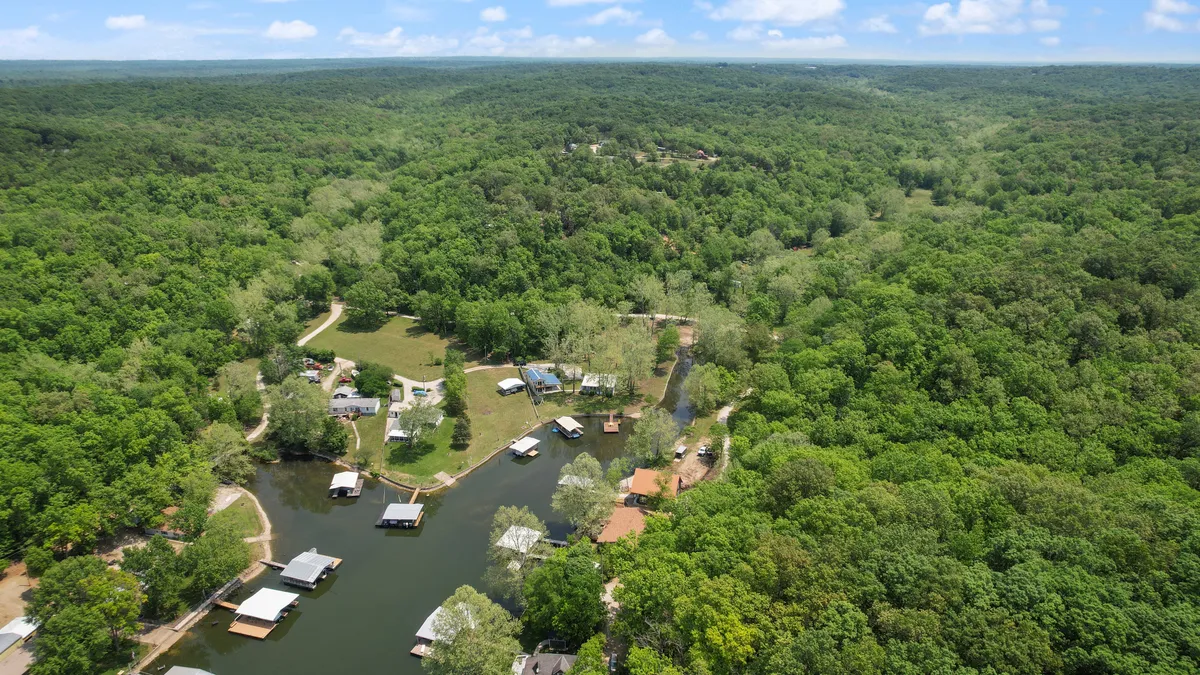 A wide view of a lush green forest and a serene waterway, with scattered houses and boathouses nestled along the shore. The setting offers a sense of seclusion and quiet, ideal for those seeking a peaceful lakeside retreat.